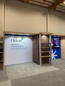 RENTAL: Modified RE-2103 Inline Design with Gravitee Panel System Backwall, Custom Hardrock Maple Laminated Soffits with Recessed Puck Lights, Extrusion Supported Laminated Shelving, Large Monitor Mount, 85" Monitor with HDMI Cable, SEG Fabric Graphics